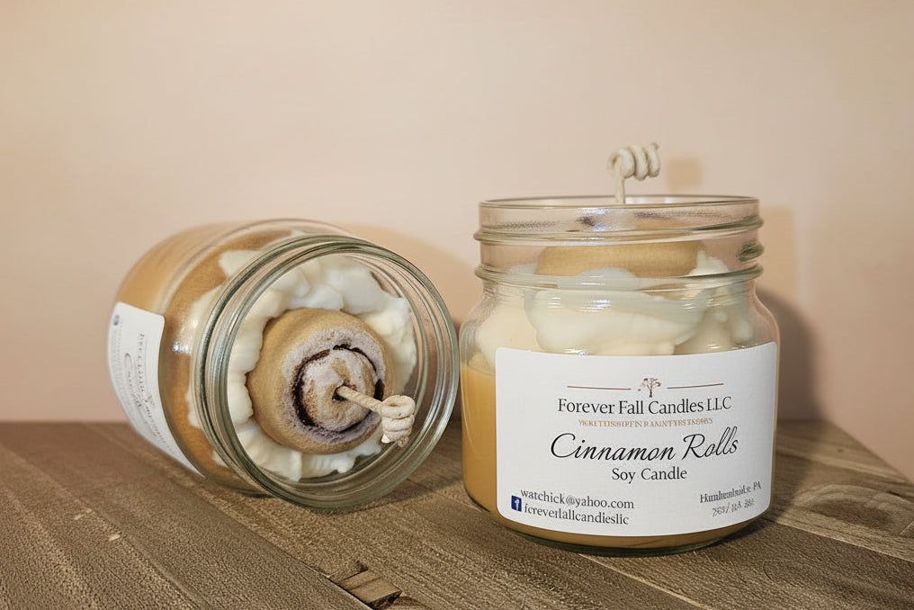 Candle in a glass jar labeled 'Cinnamon Rolls' by Forever Fall Candles LLC on a wooden surface.