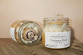 Candle in a glass jar labeled 'Cinnamon Rolls' by Forever Fall Candles LLC on a wooden surface.