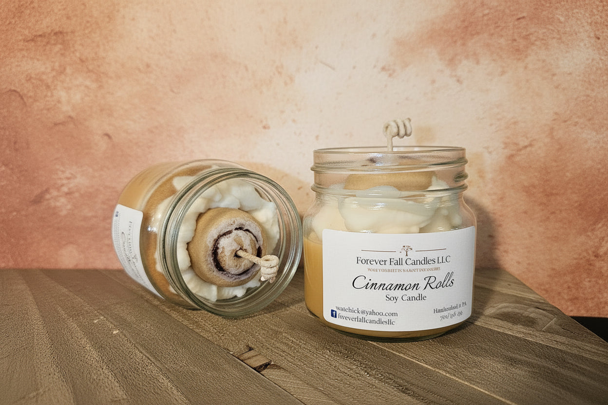 Candle in a glass jar labeled 'Cinnamon Rolls' by Forever Fall Candles LLC on a wooden surface.